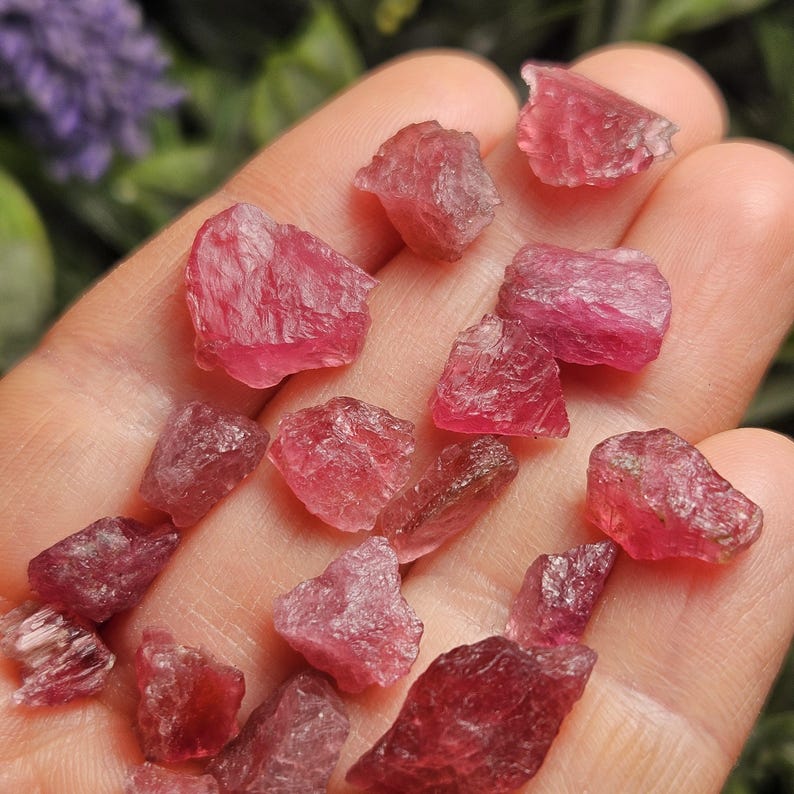May include: A collection of small, raw, unpolished pink tourmaline gemstones with irregular shapes and translucent, crystalline textures. These vibrant, deep pink mineral fragments display natural facets and jagged edges across their surfaces.
