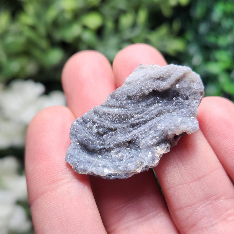 May include: A close-up of a gray and white banded agate with a smooth, polished surface. The agate has a natural, organic shape and is a beautiful example of this type of gemstone.