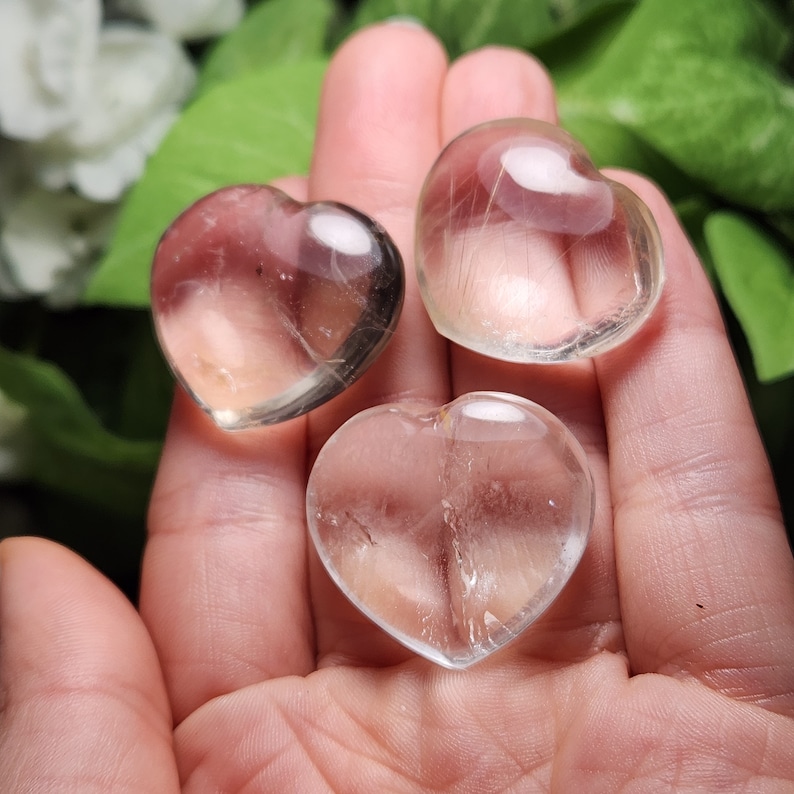 May include: Three clear quartz crystal hearts. The hearts are smooth and polished, with a slight shimmer.
