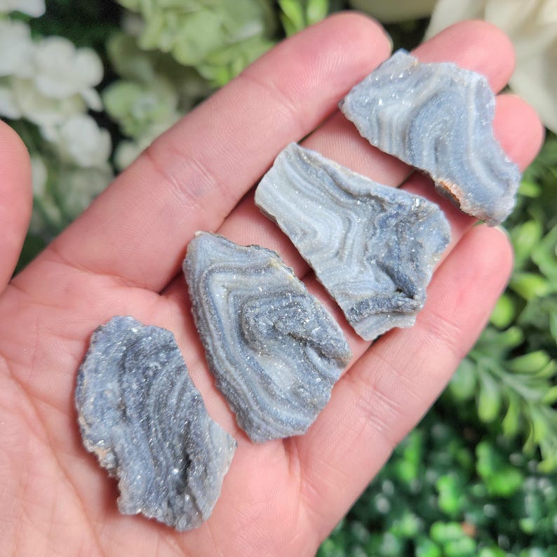 May include: Four pieces of banded agate, also known as layered agate, with a gray and white color scheme. The agate is translucent and has a natural, rough texture.