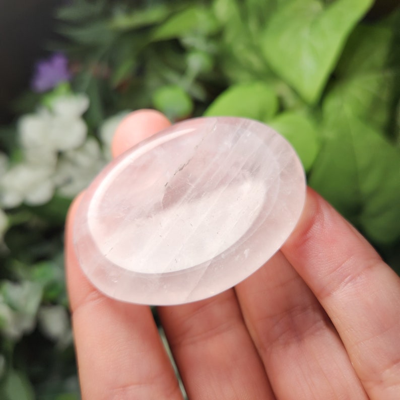 May include: A smooth, white, oval-shaped crystal with a polished surface. The crystal is translucent and has a slight pink hue.