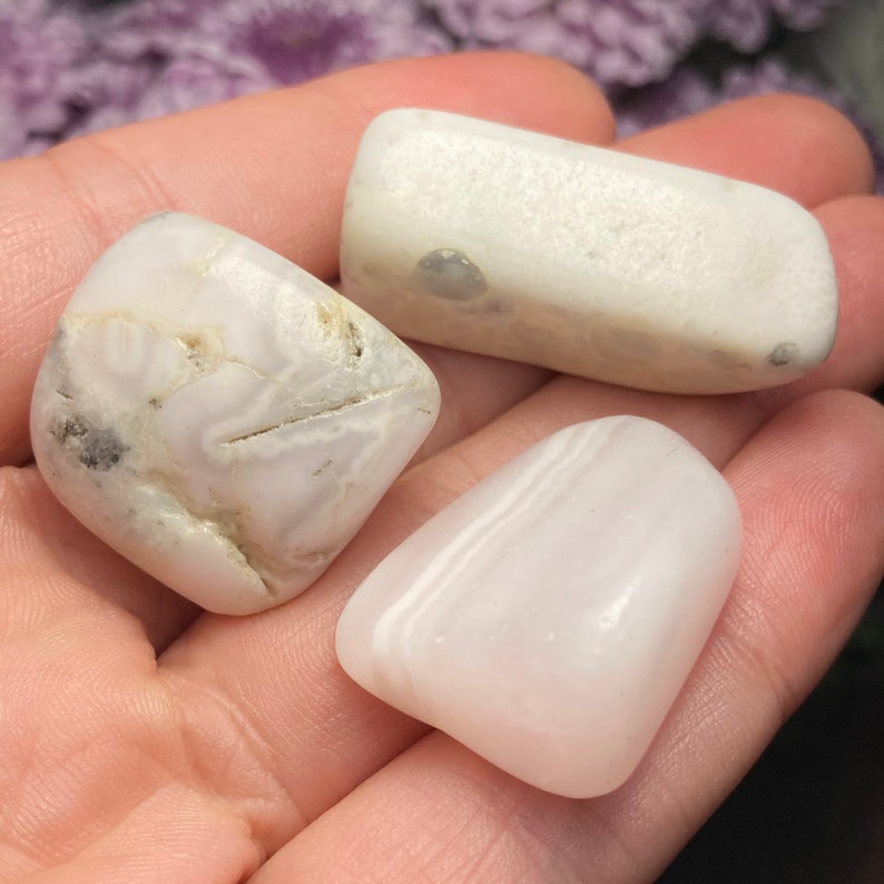 May include: Three polished stones with smooth, rounded surfaces. One stone is opaque white with grey inclusions and linear fissures, another is a rectangular white piece, and the third is a translucent, pale pinkish-white smooth stone.