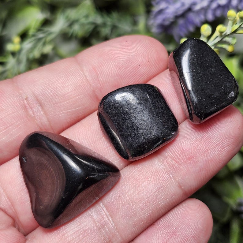 May include: Three smooth, black tumbled stones. The stones are irregularly shaped and have a glossy finish.