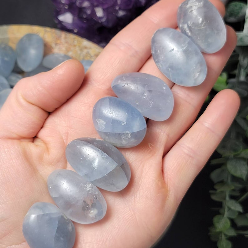May include: A collection of seven smooth, light blue, oval-shaped polished stones. The stones are arranged in a row on a hand.