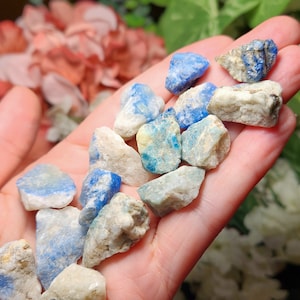 May include: A collection of small, rough, blue and white crystals. The crystals are various shapes and sizes and have a natural, raw look.