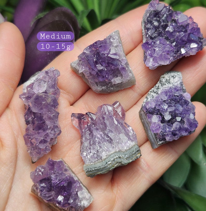Pode incluir: Seis aglomerados de cristais de ametista de tamanhos e formas variados, variando de 10 a 15 gramas. Os cristais s&atilde;o de cor roxo escuro e t&ecirc;m uma textura natural e &aacute;spera.  M&eacute;dio.