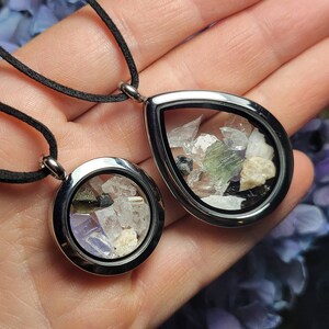 May include: Two silver locket necklaces with black cords. The lockets are open and filled with small pieces of various crystals and stones.