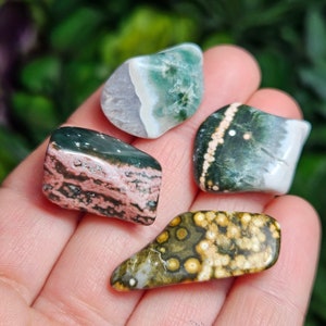 May include: Four tumbled stones with different patterns and colors. The stones are green, white, pink, and brown with white and yellow spots.