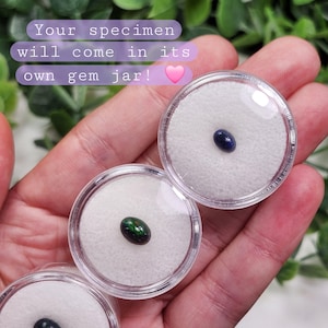 May include: Small, clear gem jars with oval-shaped gemstones. One gem is dark blue, and another is green with iridescent qualities. The text in the image reads: "Your specimen will come in its own gem jar!"
