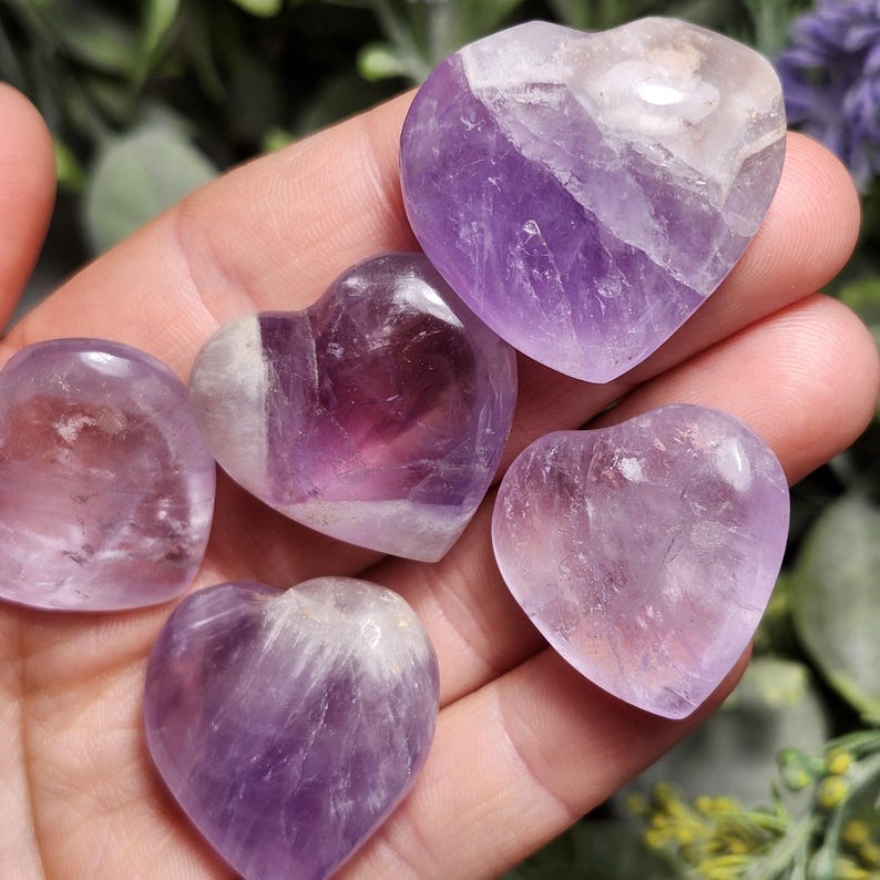 Puede incluir: Cinco cristales de amatista en forma de coraz&oacute;n, pulidos y lisos, con diferentes tonos de morado y blanco.