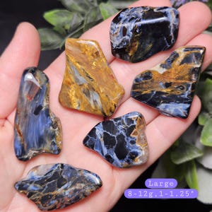 May include: Six polished pietersite stones with swirling patterns of deep blue, black, and golden-brown. The stones are irregular in shape and smooth. A purple label indicates the size as Large, 8-12g, and 1-1.25 inches in length.