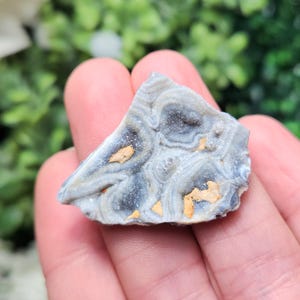 May include: A close-up of a gray and white agate with a swirling pattern and hints of gold. The agate is a natural stone with a unique and beautiful texture.