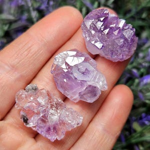 May include: Three amethyst crystal clusters in various sizes and shades of purple. The crystals are translucent and have a natural, rough texture.
