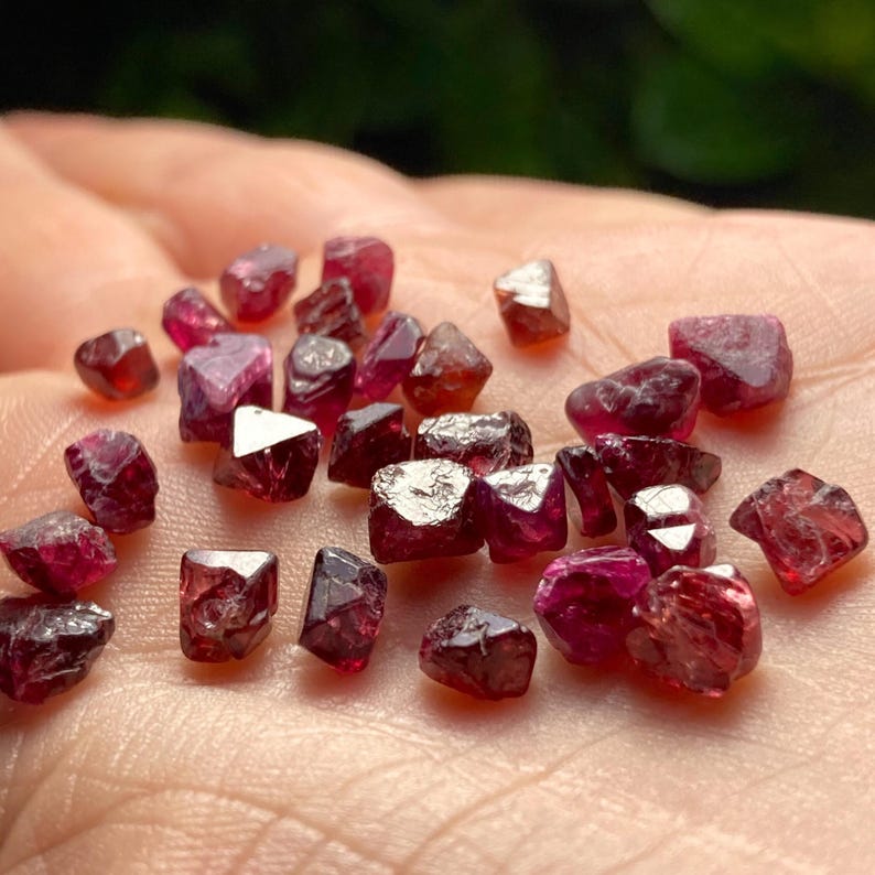 May include: A collection of small, faceted, red gemstones. The gemstones are various shades of red and have a shiny, polished finish.
