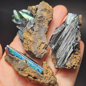 Op de afbeelding: Close-up van verschillende mineraalmonsters. De mineralen vertonen een reeks kleuren, waaronder diepblauw, groen en zwart, met een metallic glans. De mineralen zijn ingebed in een matrix van bruin en bruinachtig gesteente.