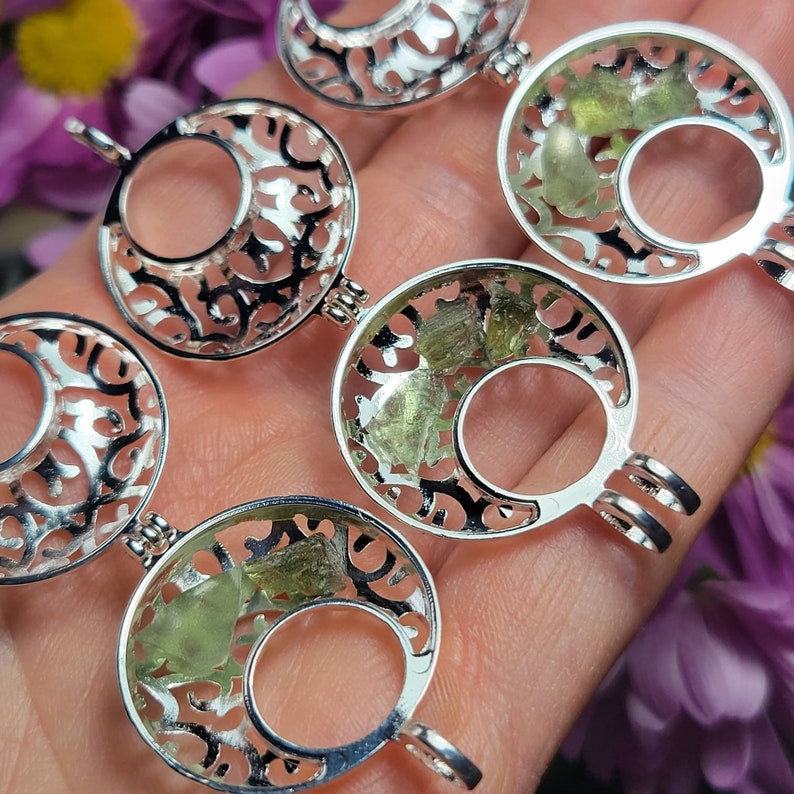 May include: Four silver locket pendants with intricate filigree designs. Each locket contains green crystals.