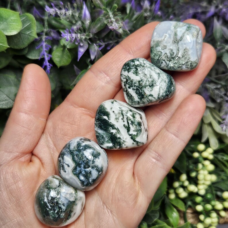 May include: Five polished moss agate stones arranged in a line. Each stone features a smooth, rounded surface with a distinct pattern of deep forest green inclusions set against a translucent, milky white and grey crystalline base material.