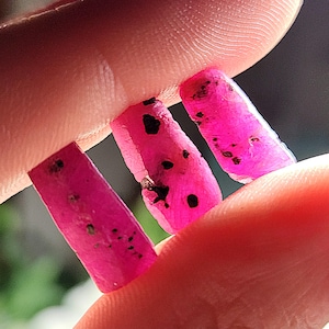 Könnte beinhalten: Drei rosafarbene Rubinkristalle mit schwarzen Einschlüssen, in einer Hand gehalten.