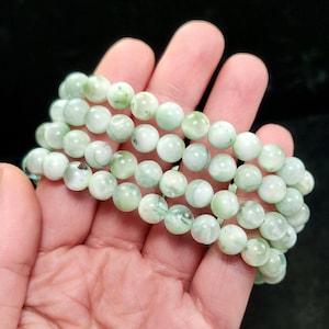 Peut inclure: Trois rang&eacute;es de bracelets de perles vert clair. Les perles rondes ont un aspect marbr&eacute; avec des variations de couleur. Les bracelets sont tenus dans une main sur fond noir. Les perles mesurent environ 0,8 cm de diam&egrave;tre.