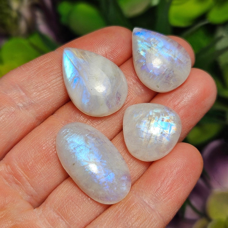May include: Four iridescent moonstone cabochons in teardrop and oval shapes. The stones are a milky white color with a blue sheen.