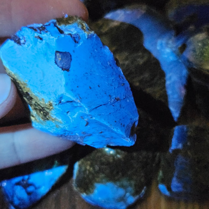 May include: A collection of blue and black stones with a rough, natural texture. The stones are illuminated with a blue light, highlighting their unique patterns and shapes.