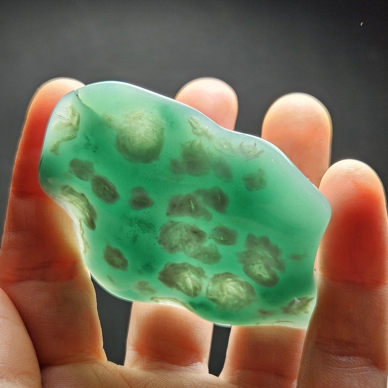 May include: A green, translucent, irregularly shaped stone with white inclusions. The stone is smooth and polished.