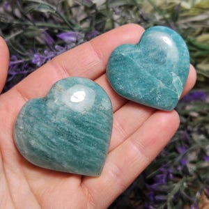 Peut inclure: Deux pierres d'amazonite en forme de c&oelig;ur de couleur verte. Les pierres sont lisses et polies, avec une couleur vert clair et des stries blanches.