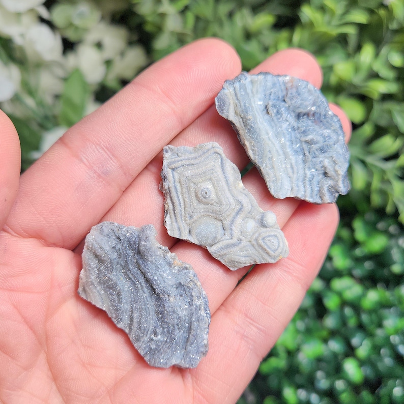 May include: Three gray and white agate stones with different patterns. The stones are smooth and have a natural, polished look.