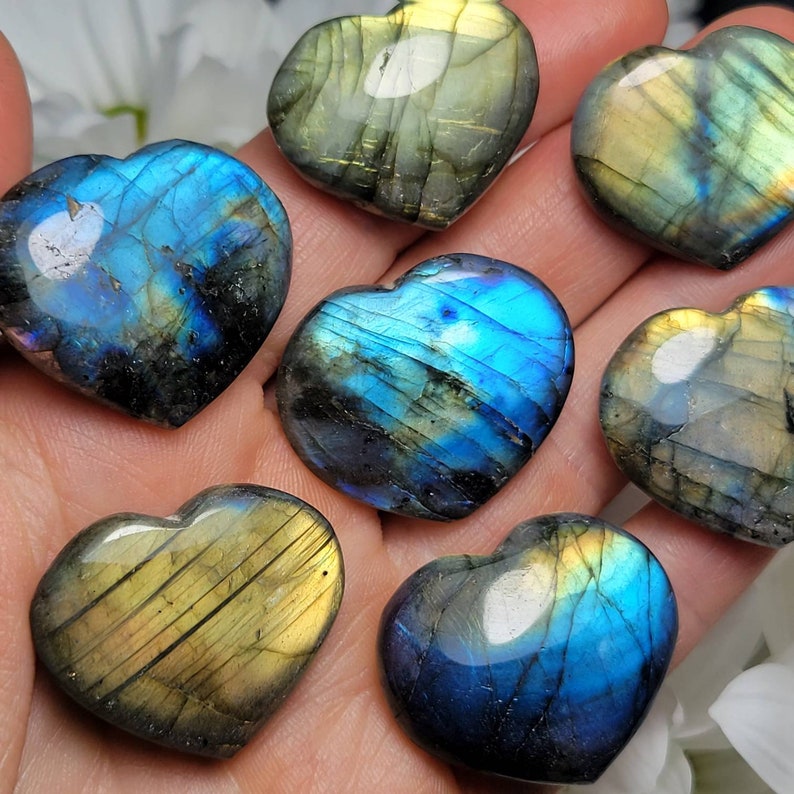 May include: Seven heart-shaped labradorite crystals in various shades of blue, green, and gold. The crystals are polished and have a iridescent sheen.