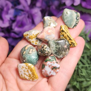 May include: A collection of polished ocean jasper tumbled stones in various shades of green, brown, white, and pink with intricate patterns.