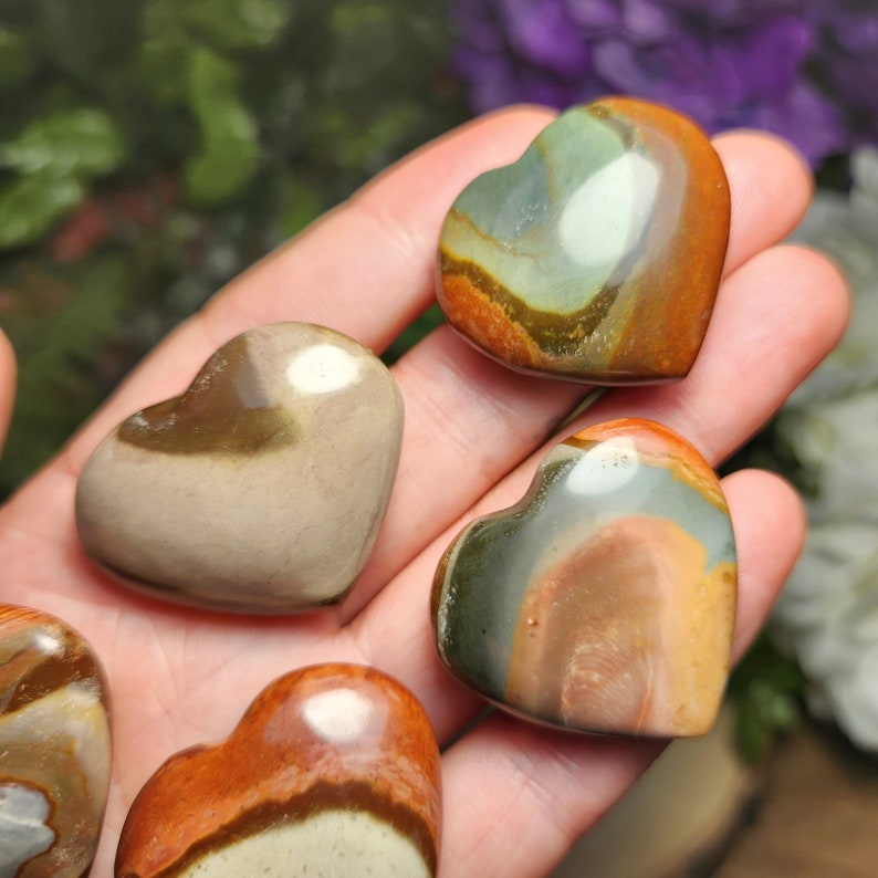 May include: Four heart-shaped polished stones with brown, green, and white patterns. The stones are arranged in a hand.