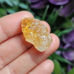 May include: A raw, unpolished citrine crystal featuring a translucent, golden-yellow hue with natural crystalline facets and a jagged, irregular shape. The stone displays varying levels of clarity, transitioning from a deep amber tone to clear.