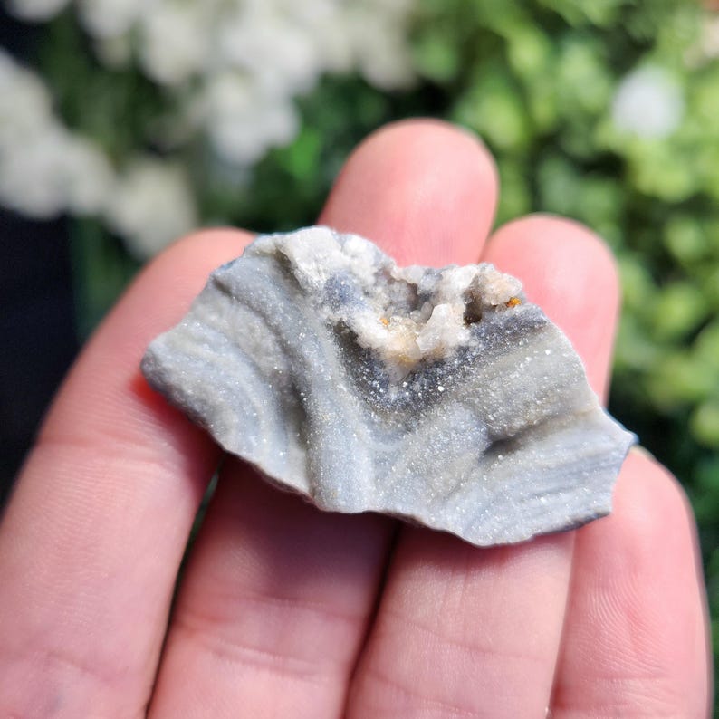 May include: A small, gray and white agate geode with a rough, natural exterior and a crystal-lined interior. The geode is about the size of a hand.