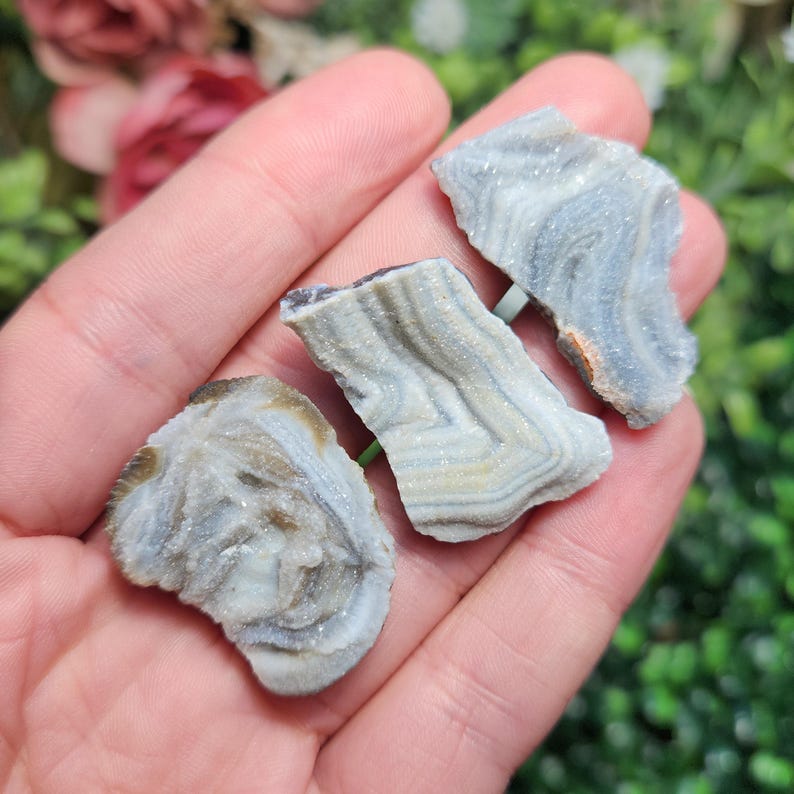 May include: Three pieces of banded agate with white and gray banding. The agate is translucent and has a crystalline texture.