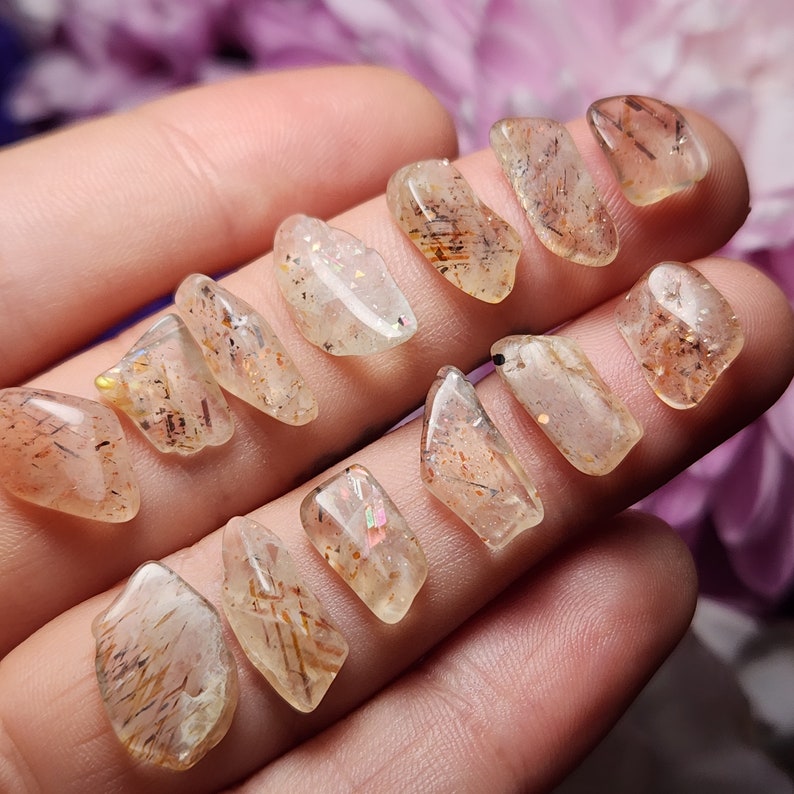 May include: A selection of clear, polished gemstones with internal inclusions. The stones are a light amber colour with dark brown and gold streaks. The gemstones are irregularly shaped and appear to be held in a hand.