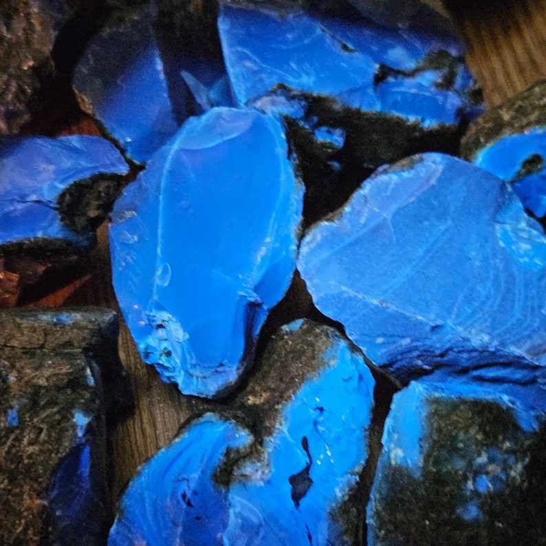 May include: A close-up of several pieces of blue, translucent, polished stone. The stones are irregularly shaped and have a smooth, glassy surface.