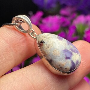 May include: A silver pendant with a teardrop-shaped purple and white opal stone. The pendant is on a silver chain.