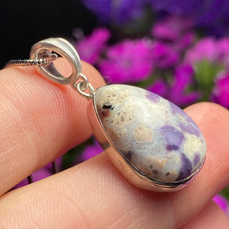 May include: A silver pendant with a teardrop-shaped purple and white opal stone. The pendant is on a silver chain.