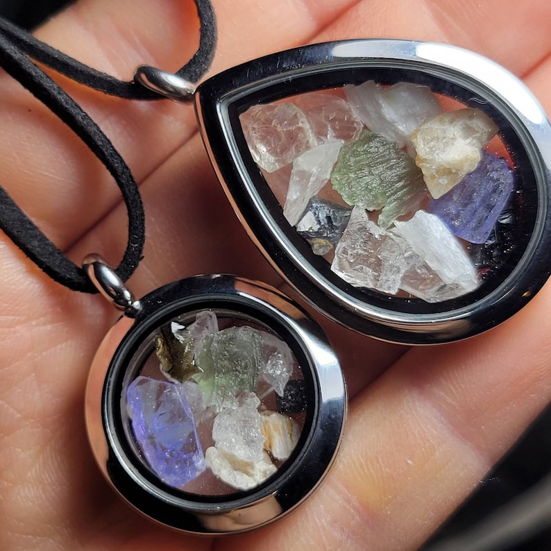 May include: Two silver locket necklaces with different sized round pendants. The pendants contain a variety of small, colorful crystals and stones.