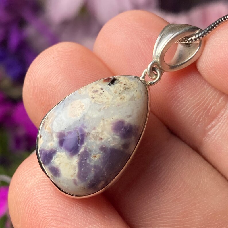 May include: A teardrop-shaped pendant with a silver bail and a purple and white opal stone.