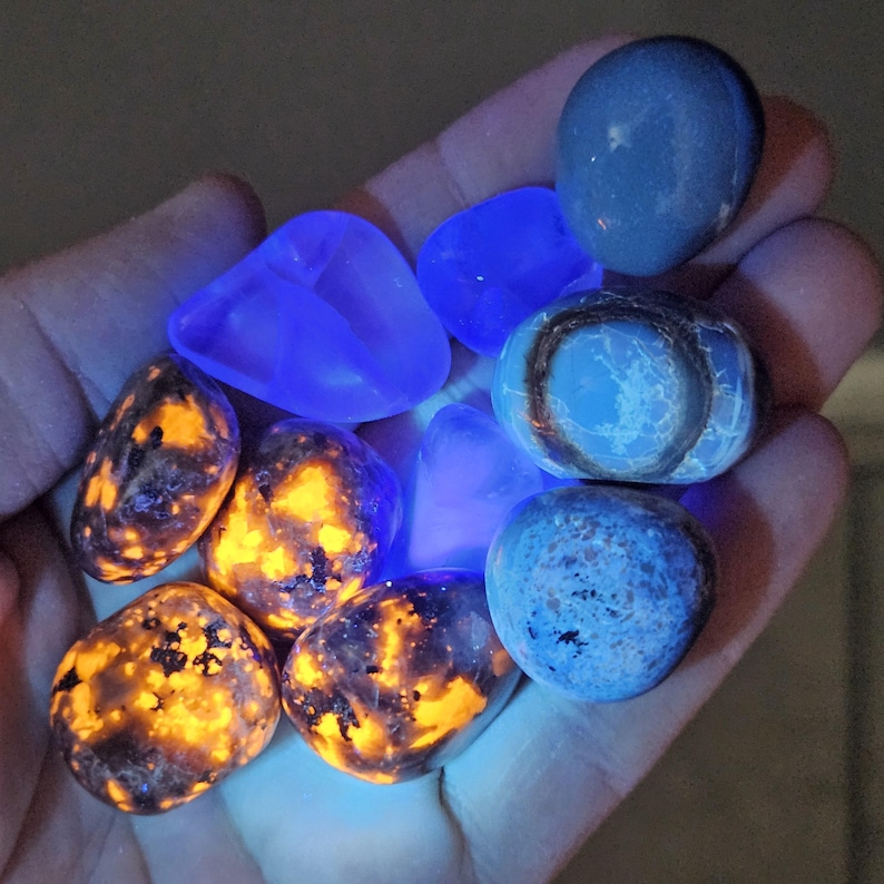 May include: A collection of glowing rocks and stones in various shapes and sizes. Some stones have a bright orange and yellow interior, while others are blue or gray. The stones are held in a hand, with a dark background.