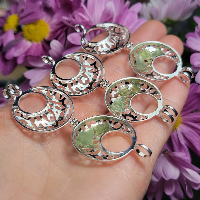 May include: Five silver locket pendants with intricate filigree designs. Each pendant features a crescent moon shape with a clear glass window revealing green crystals inside.