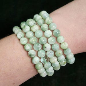 Peut inclure: Plusieurs bracelets de perles vert clair. Les bracelets sont compos&eacute;s de perles rondes et polies avec un aspect marbr&eacute;. Les perles pr&eacute;sentent diff&eacute;rentes nuances de vert et de blanc. Les bracelets sont port&eacute;s au poignet.