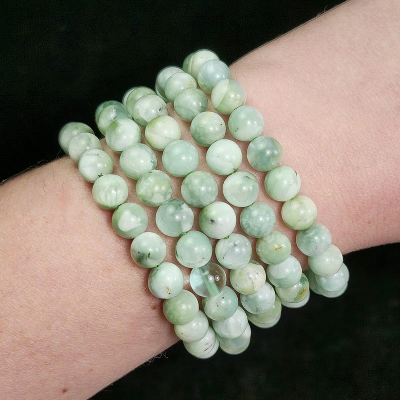 Peut inclure: Plusieurs bracelets de perles vert clair. Les bracelets sont compos&eacute;s de perles rondes et polies avec un aspect marbr&eacute;. Les perles pr&eacute;sentent diff&eacute;rentes nuances de vert et de blanc. Les bracelets sont port&eacute;s au poignet.