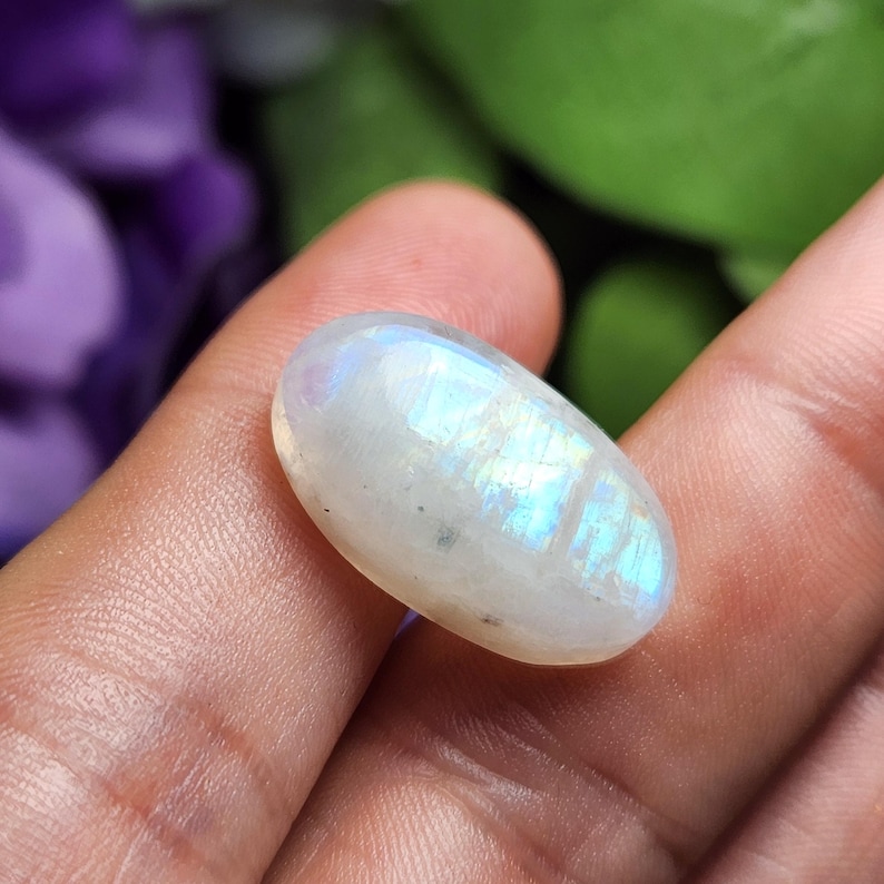 May include: Oval shaped moonstone cabochon with a white base and iridescent blue and green flashes.