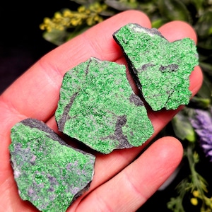 May include: Three irregular, flat mineral specimens featuring a vibrant, crystalline green surface texture contrasted with dark, matte gray stone sections. These raw, jagged-edged rock fragments display a natural, granular appearance with deep green hues.