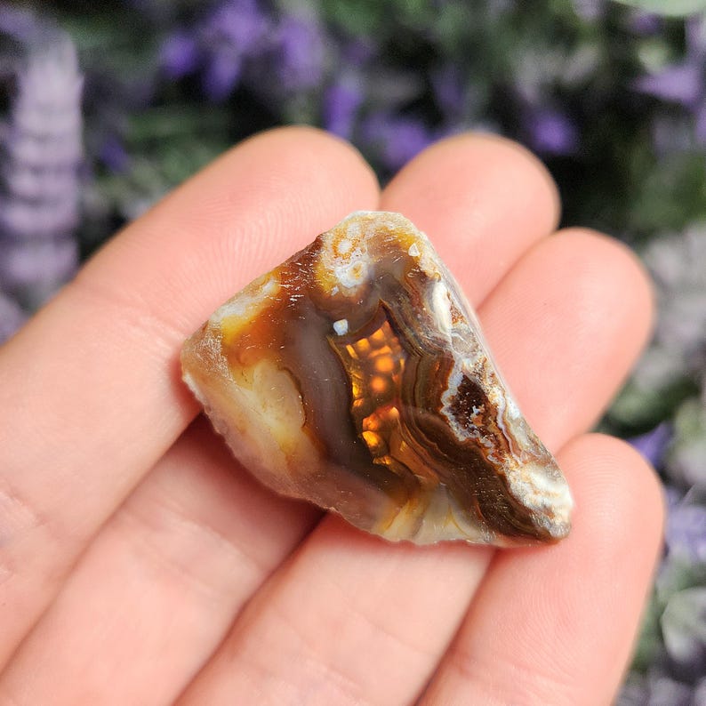May include: A close-up of a brown, white, and orange agate stone with a banded pattern. The stone is smooth and polished.