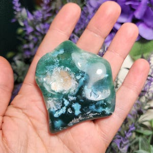 May include: A green, blue, and white agate stone with a smooth, polished surface. The stone has a unique, swirling pattern and is a natural, organic shape.