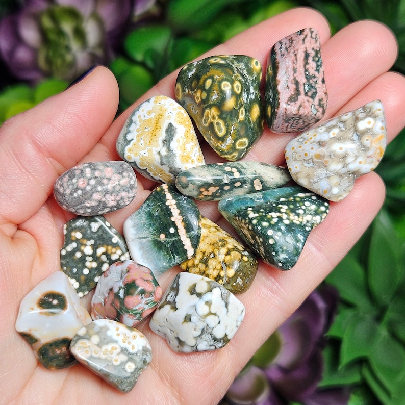 May include: A collection of tumbled ocean jasper stones in various shades of green, brown, white, and pink. The stones have a unique speckled pattern and are smooth to the touch.
