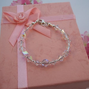May include: A delicate silver bracelet with clear crystal beads, displayed in a pink gift box with a satin ribbon.